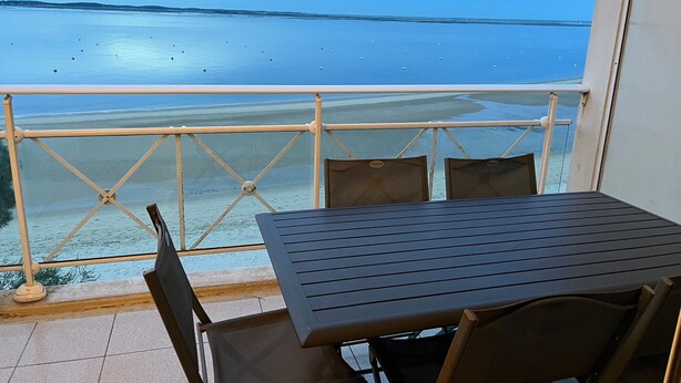Ein Balkon mit Tisch und Stühlen mit Blick auf ein ruhiges Meer und einen Sandstrand.