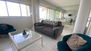Ein großzügiger Wohnbereich mit grauem Sofa, blaugrünen Sessel und einem Glastisch.