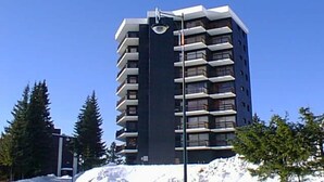 Een meerlaags gebouw met balkons, omringd door bomen en sneeuw.