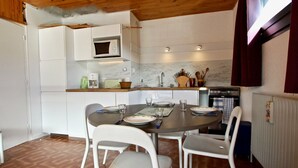Een kleine keuken met witte kastjes, een magnetron, en een eethoek met vier witte stoelen en een ronde tafel.