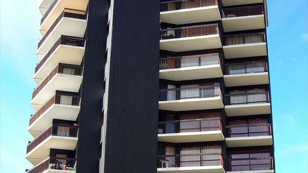 Een hoog gebouw met meerdere balkons, elk voorzien van een leuning en ramen.