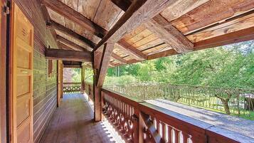 Une véranda en bois, dotée d’une balustrade, qui donne accès à une zone boisée.