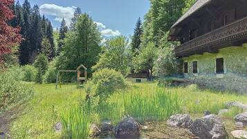 Un chalet rustique doté d’un balcon, entouré d’un jardin luxuriant et d’un petit étang.