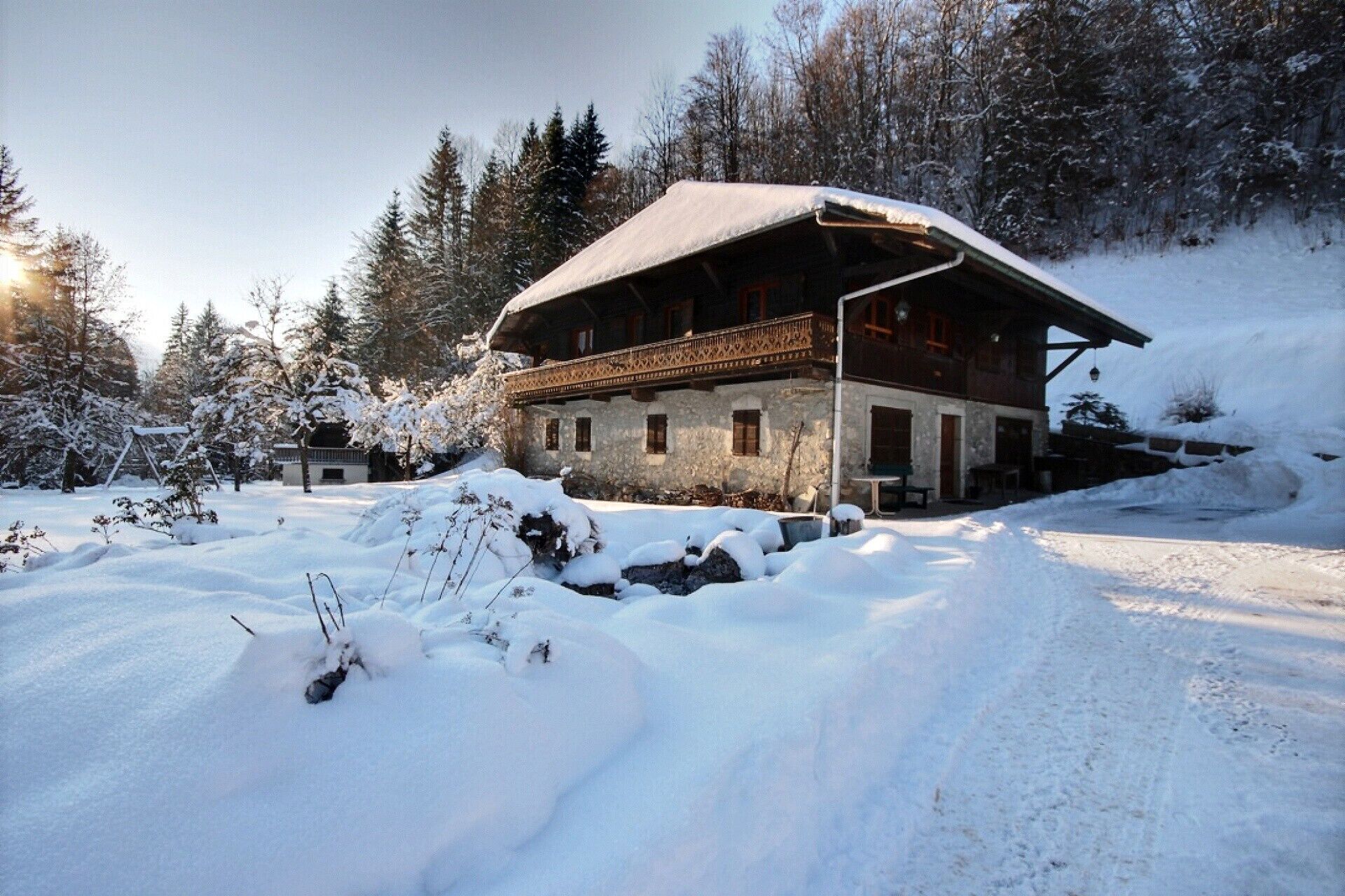 Un chalet en bois, doté d’un toit à pente, entouré d’arbres couverts de neige et surplombé par un ciel dégagé.