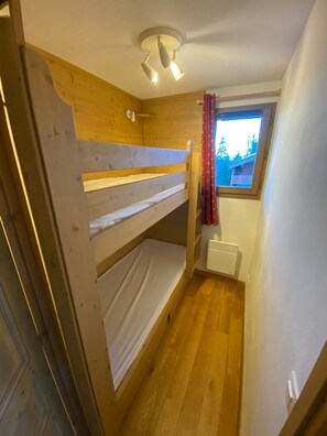 A small, compact room with a bunk bed, a window with a view, and a ceiling light fixture.