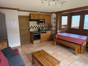 A compact kitchen with wooden cabinets, a microwave, and a dining area with a checkered tablecloth. - C301 - 60 m2 - 3P+Cab - 6/8 pers (Prapoutel)