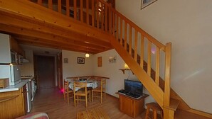 A cozy living room with a wooden staircase, a dining area, and a kitchen. - Apt 2BR + loft for 6 - ski-in/ski-out - garage - WIFI (Le Grand-Bornand)