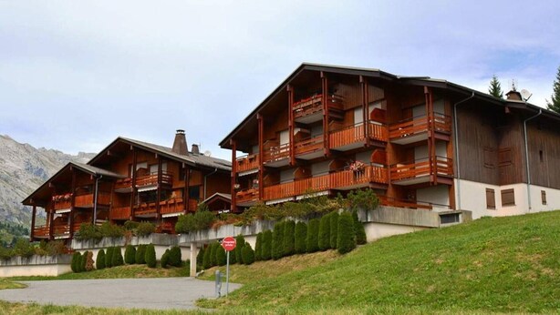 A multi-story wooden building with balconies, set against a mountainous backdrop. - Apt 2BR + loft for 6 - ski-in/ski-out - garage - WIFI (Le Grand-Bornand)