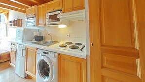 A compact kitchen with wooden cabinets, a microwave, a stove, a sink, and a washing machine. - Apt 2BR + loft for 6 - ski-in/ski-out - garage - WIFI (Le Grand-Bornand)