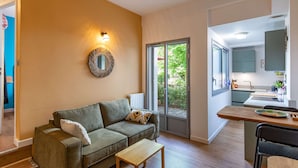 A modern living room with a sofa, a small table, a mirror, and a kitchen area with a window.