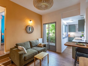 A modern living room with a sofa, a small table, a mirror, and a kitchen area with a window.