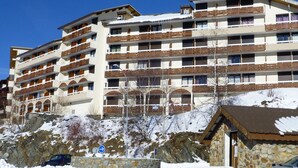 A multi-story hotel with balconies, a stone facade, and a ski slope in the background. - Cozy 1-Bedroom Apartment for 5 with South-Facing Balcony in L'Alpe d'Huez (Huez)