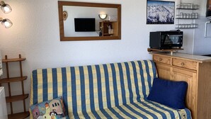 A cozy living room with a striped sofa, a small wooden cabinet, a television, and a framed picture on the wall. - Cozy 1-Bedroom Apartment for 5 with South-Facing Balcony in L'Alpe d'Huez (Huez)