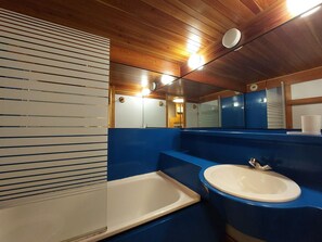 Une salle de bain avec un plafond en bois, un mur bleu, un lavabo blanc et une baignoire blanche.