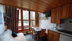 A compact room with a bed, a small dining table, wooden cabinets, a built-in oven, and a large window with curtains. - Cozy duplex for 4 near slopes at Arcs 1800 (Les Arcs 1800)