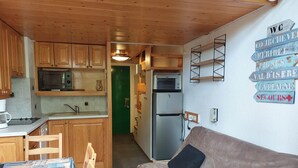 A compact kitchen with wooden cabinets, a microwave, and a refrigerator. There is a dining area with a table and chairs, and a sofa in the living area. - Cozy duplex for 4 near slopes at Arcs 1800 (Les Arcs 1800)