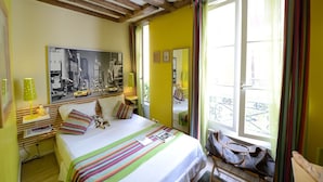 Habitación de hotel con cama, un cuadro de paisaje urbano, una ventana con vistas y un balcón con barandilla.
