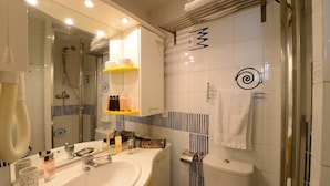 Un baño moderno con un espejo grande, un lavamanos con artículos de tocador, una ducha y azulejos decorativos.