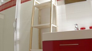 Un bagno con pareti rivestite di piastrelle bianche, un mobile lavabo rosso con due cassetti e una scala in legno.