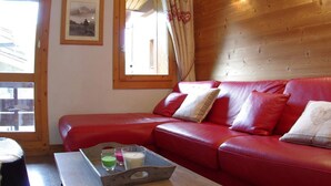 Un divano in pelle rossa con cuscini, una parete in legno, un quadro incorniciato e una finestra con tende.