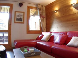 Ein rotes Ledersofa mit Kissen, eine Holzwand, ein gerahmtes Bild und ein Fenster mit Vorhängen.
