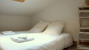 Una camera da letto con finestra sul tetto, un letto con lenzuola bianche e un contenitore in vimini.