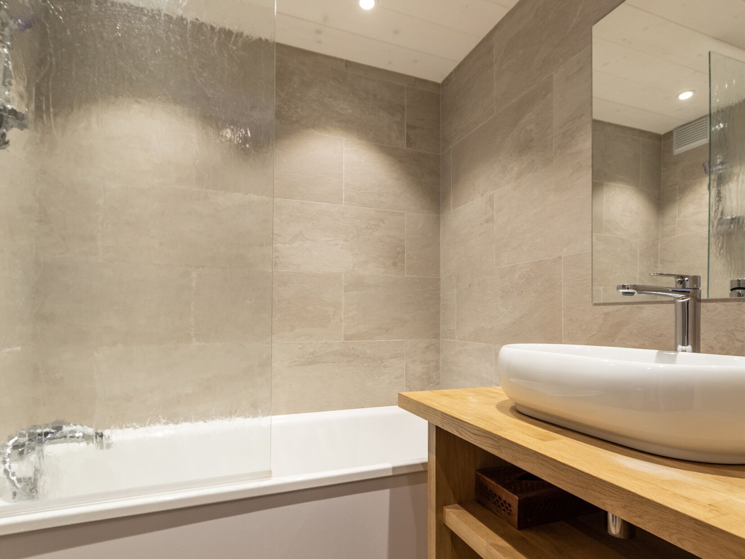 Een moderne badkamer met een vrijstaand bad, een grote spiegel en een houten wastafelmeubel.