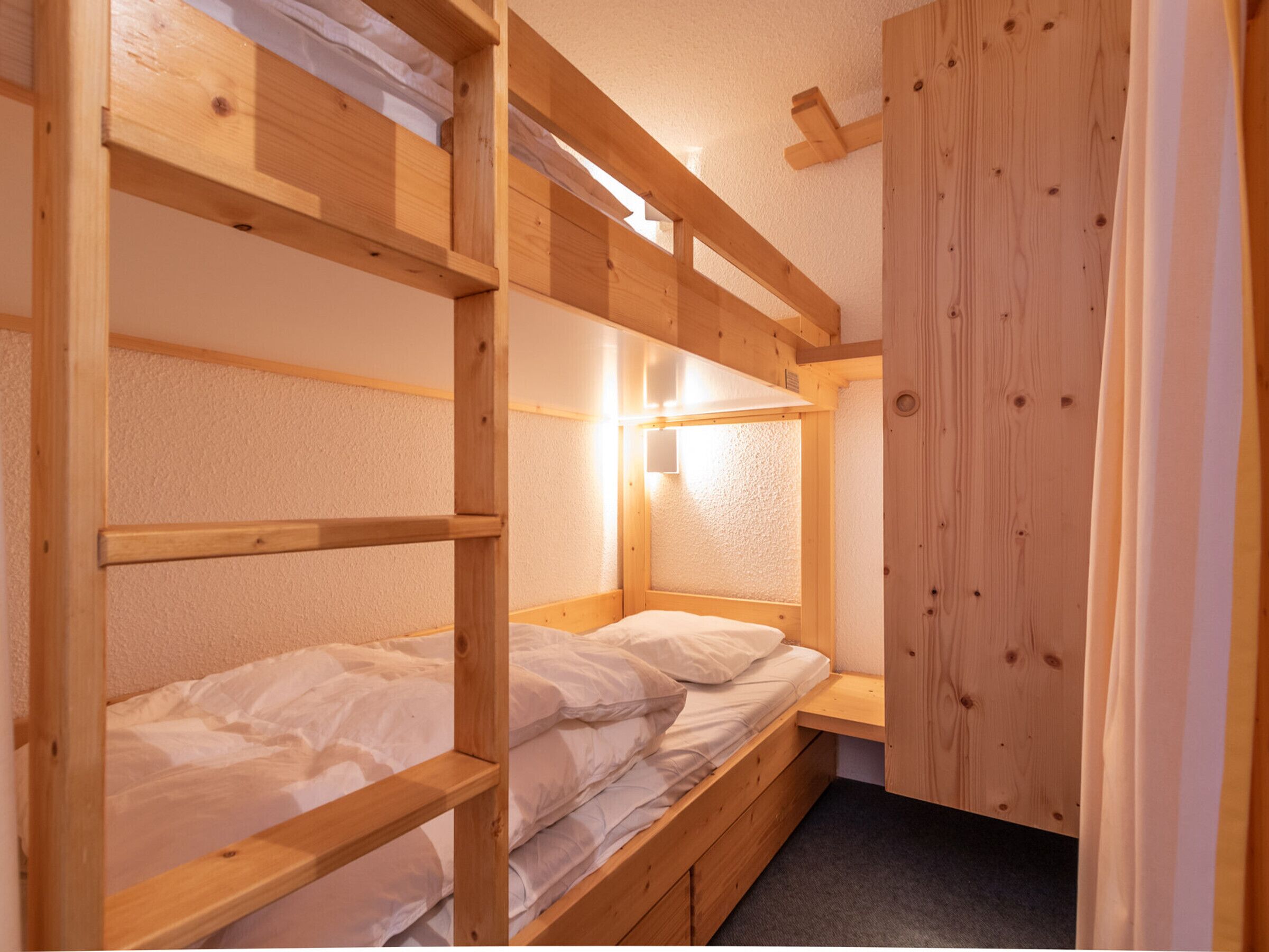 A bunk bed room with a wooden headboard, a small bedside table, and a wall-mounted light.