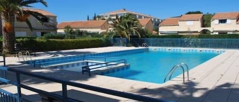A rectangular swimming pool with a blue border, surrounded by a tiled deck and a blue railing.