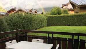 Un patio con mesa y sillas, cerca de madera, y vista a una montaña y un arcoíris.