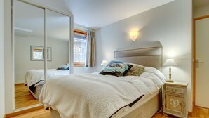 Un dormitorio con una cama grande, una mesita de noche, un espejo y vistas al exterior.