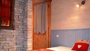 Una camera da letto con parete in pietra, porta in legno e un letto con copriletto a motivi a cuore rossi.