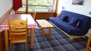 Una habitación acogedora con una mesa a cuadros, sillas de madera, un suelo estampado de pata de gallo y un sofá azul, con una ventana que da a árboles.