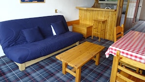 Una habitación con sofá azul, mesa de madera, mantel a cuadros, alfombra escocesa, sillas de madera, un banco de madera, un microondas y una pared verde.