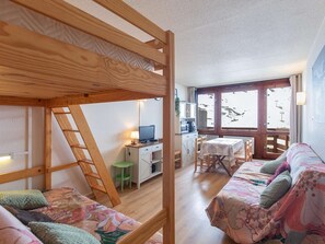 A room with a bunk bed, a desk with a computer, a dining table, and a window with a view of a snowy landscape.