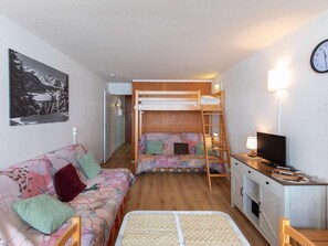 Une chambre avec un lit superposé, un canapé, un bureau avec une télévision et une horloge au mur.