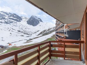 A balcony with a mountain view, a wooden railing, and a building with multiple floors.