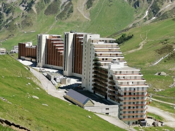 A modern multi-story hotel with a flat roof, located in a mountainous area with green hills in the background.
