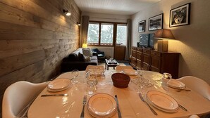 A dining area with a wooden interior, a sofa, a television, and framed pictures on the wall.