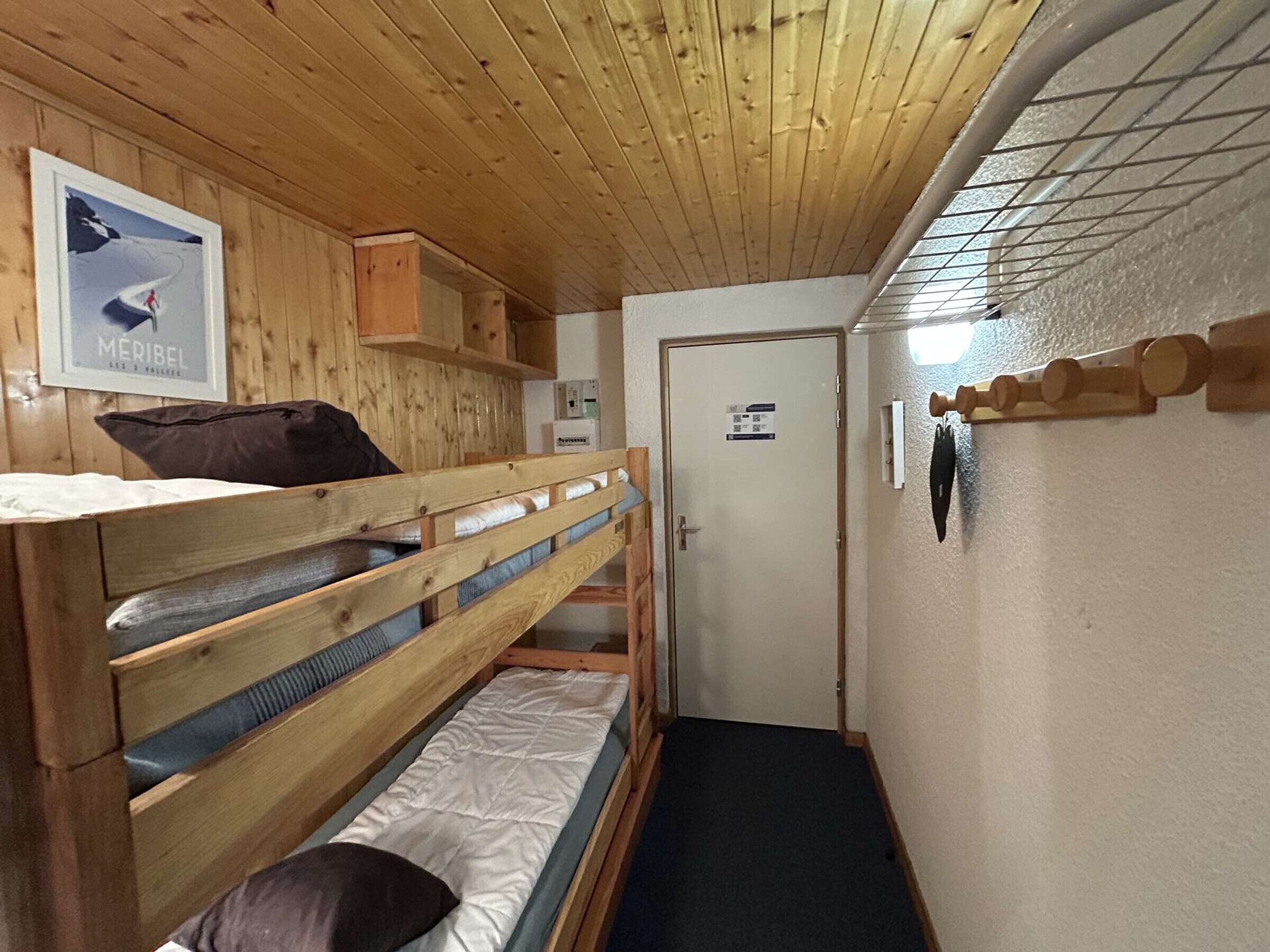 A room with bunk beds, a wooden ceiling, a door, and a framed picture on the wall.