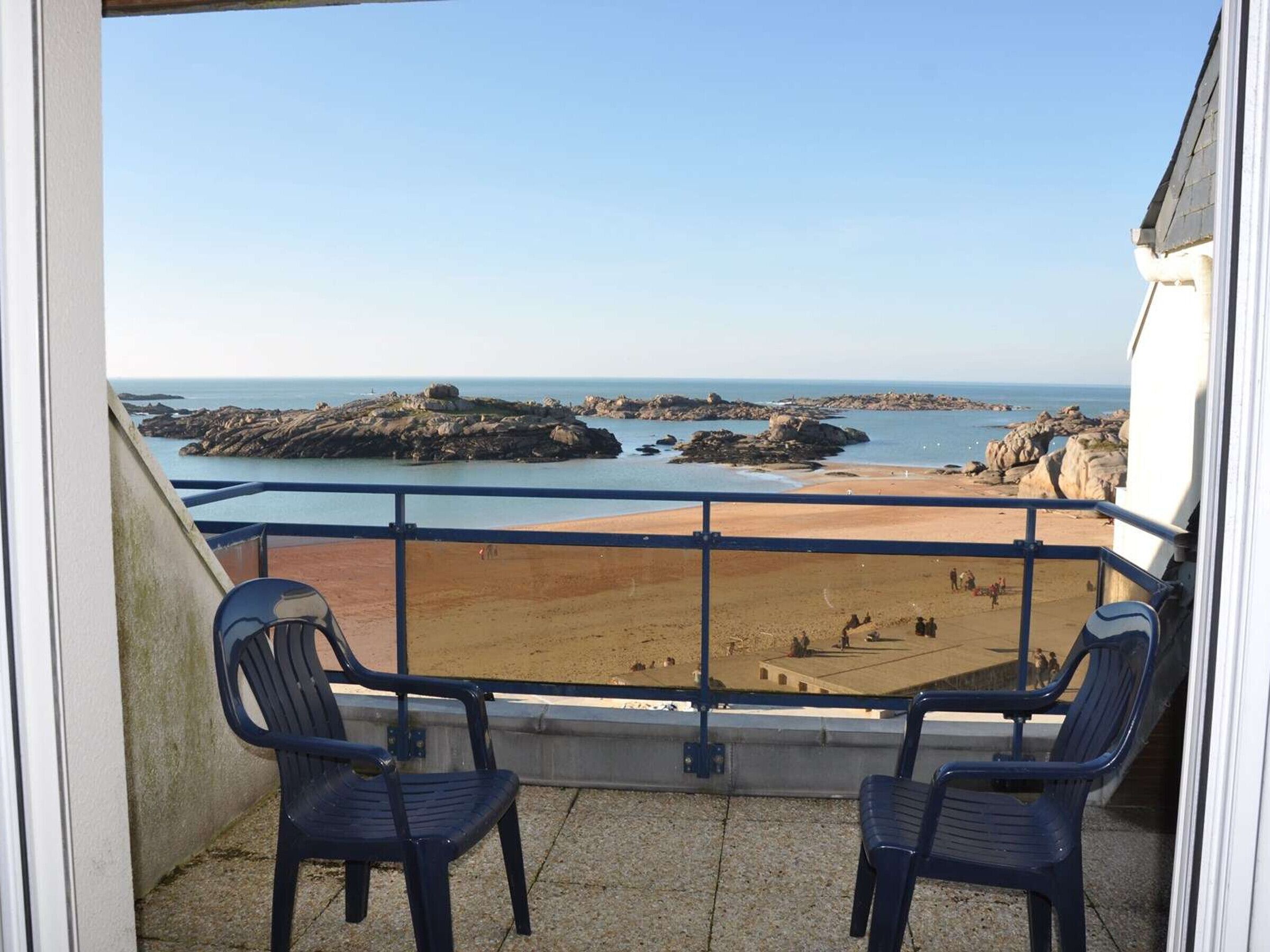 A balcony with two chairs overlooking a beach with rocky outcrops and a clear view of the sea.