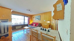 Ein gemütliches Zimmer mit Holzeinrichtung, einem Esstisch mit Stühlen, einer Couch und einem Fenster mit Vorhängen.
