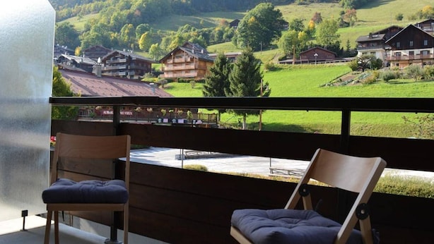 Ein Balkon mit zwei Holzstühlen und Blick auf ein Dorf mit Häusern und Bäumen.