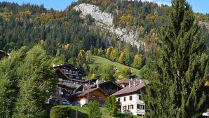 Ein Bergdorf mit traditionellen Holzhäusern, wolkenlosem Himmel und herbstlich gefärbten Bäumen.