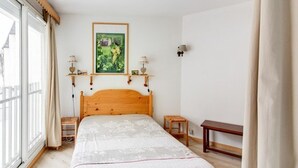 A bedroom with a wooden bed, a painting on the wall, bedside lamps, and a view of the outside. - Bright 2-room apt, sleeps 6, parking, near shops and skiing (Barèges)