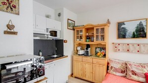 A compact kitchen with a stove, microwave, and wooden cabinets. There's a bed with a red blanket and a painting on the wall. - Bright 2-room apt, sleeps 6, parking, near shops and skiing (Barèges)