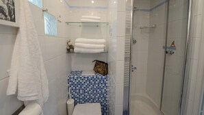 Un baño con cabina de ducha de vidrio, inodoro y lavabo. Hay toallas en un estante y un cuadro en la pared.