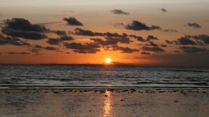 A sunset over a beach with the sun partially obscured by clouds.