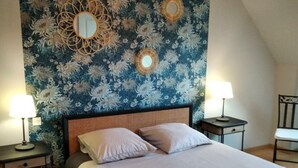 A bedroom with a large bed, two bedside tables with lamps, a chair, and a decorative wall with floral patterns and mirrors.