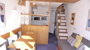 A compact living space with a wooden dining table, a sofa, a kitchen area with a microwave and stove, and a staircase leading to another level. - 3-room duplex sleeps 6 near slopes in Arc 1800 (Les Arcs 1800)